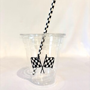 Puede incluir: Un vaso de pl&aacute;stico transparente con tapa, con dos banderas de carreras a cuadros en blanco y negro cruzadas. Una pajita de papel a cuadros en blanco y negro est&aacute; insertada en el vaso. El vaso est&aacute; dise&ntilde;ado para bebidas fr&iacute;as.