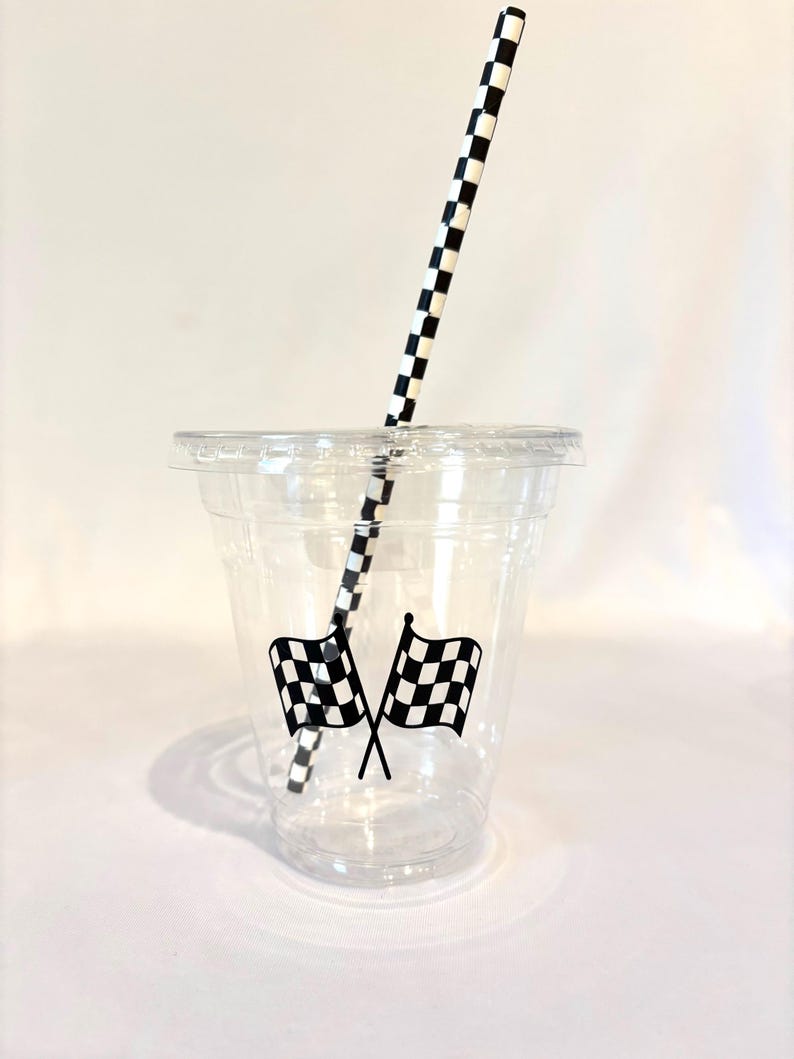 Puede incluir: Un vaso de pl&aacute;stico transparente con tapa, con dos banderas de carreras a cuadros en blanco y negro cruzadas. Una pajita de papel a cuadros en blanco y negro est&aacute; insertada en el vaso. El vaso est&aacute; dise&ntilde;ado para bebidas fr&iacute;as.