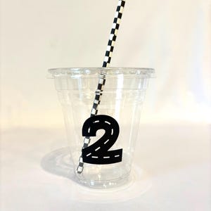Puede incluir: Un vaso de pl&aacute;stico transparente con tapa, con un n&uacute;mero 2 negro con dise&ntilde;o de carretera. Una pajita a cuadros blancos y negros est&aacute; insertada en el vaso. La taza est&aacute; dise&ntilde;ada para una fiesta de cumplea&ntilde;os.