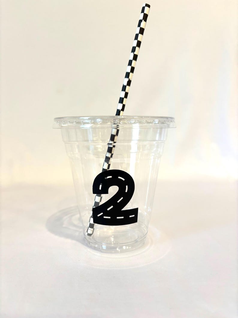 Puede incluir: Un vaso de pl&aacute;stico transparente con tapa, con un n&uacute;mero 2 negro con dise&ntilde;o de carretera. Una pajita a cuadros blancos y negros est&aacute; insertada en el vaso. La taza est&aacute; dise&ntilde;ada para una fiesta de cumplea&ntilde;os.