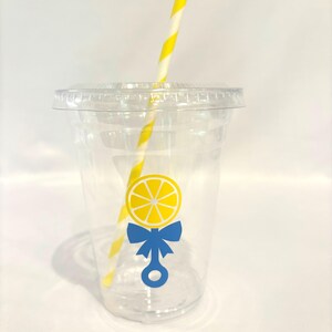 May include: Clear plastic cup with a lid and a yellow and white striped straw. The cup features a lemon design with a blue bow and rattle graphic. Suitable for cold drinks.
