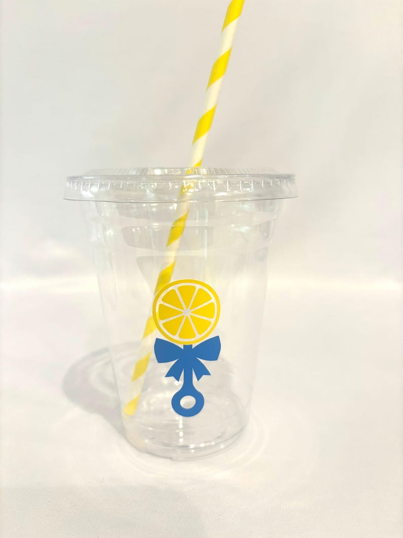May include: Clear plastic cup with a lid and a yellow and white striped straw. The cup features a lemon design with a blue bow and rattle graphic. Suitable for cold drinks.