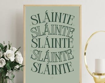May include: A framed print with the word "SLÁINTE" repeated five times in a dark green, stylized font. The background is a muted green colour. The frame is a light wood colour. A bouquet of white roses is visible on the left.