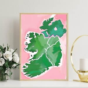 Puede incluir: Una impresión artística enmarcada que presenta un mapa estilizado de Irlanda. El mapa está pintado en tonos verdes, con líneas blancas que delinean los condados, sobre un fondo rosa. La obra de arte está en un marco de madera.