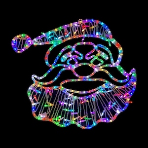 May include: A colorful Christmas decoration in the shape of Santa Claus's face. The outline is made of a flexible, white material, and is illuminated with a multitude of small, multi-colored LED lights. The background is solid black.