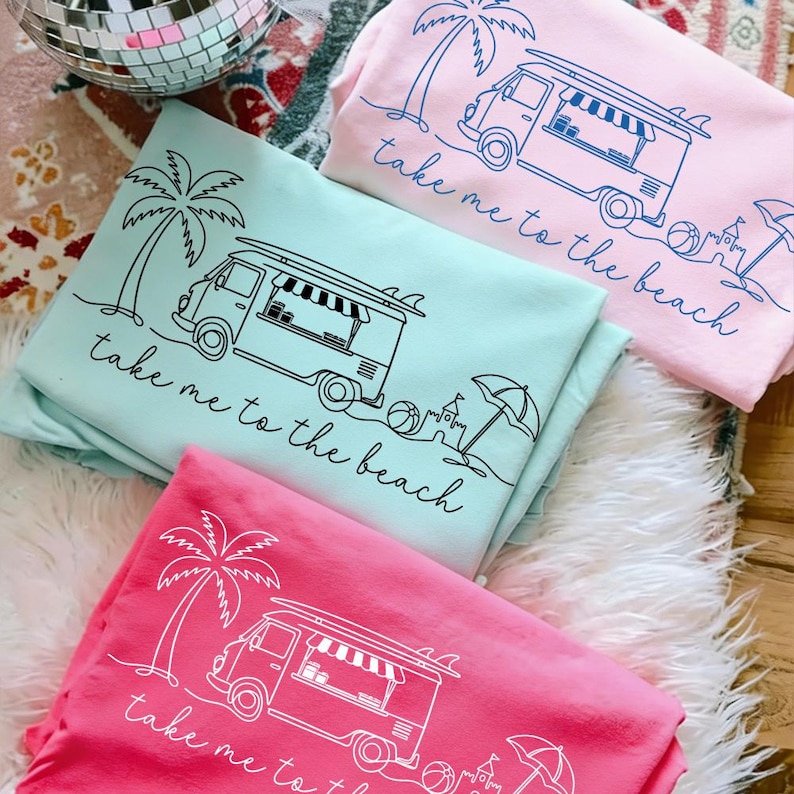 May include: Three sweatshirts in shades of pink and teal, each featuring a beach-themed graphic. The design includes a palm tree, a van with a surfboard, and the phrase "take me to the beach."
