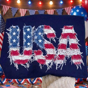 May include: A navy blue textile with the word "USA" appliqu&eacute;d in red, white, and blue fabric. The letters have a distressed, frayed edge, and the "U" and "S" feature white stars.