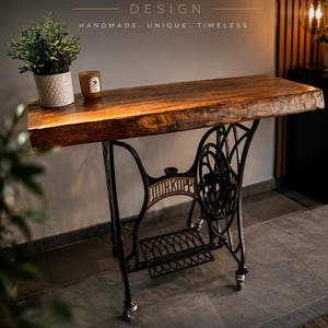 May include: A console table featuring a thick, natural-edge wooden slab top supported by a repurposed black cast-iron sewing machine base with wheels. The base displays the brand name Dürkopp. Text O.LIVE DESIGN HANDMADE. UNIQUE. TIMELESS. is visible.
