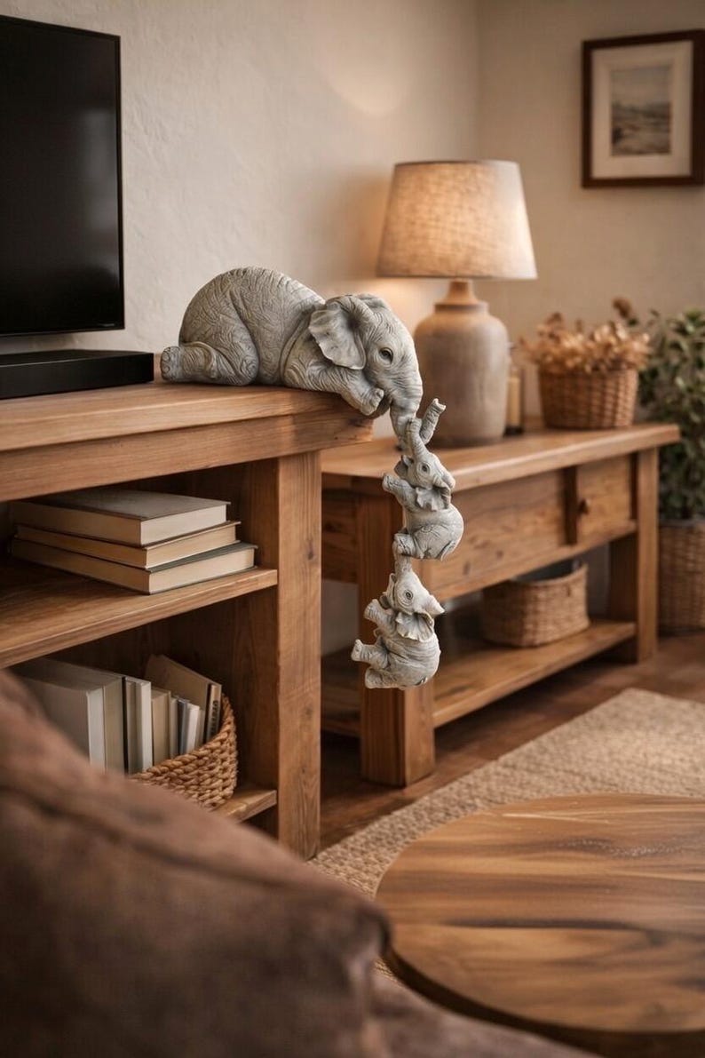 May include: A gray elephant family sculpture. The largest elephant rests on a wooden surface, with three smaller elephants hanging below, each holding the tail of the one above. The sculpture is a decorative accent for a home.