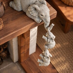 May include: A gray elephant figurine with three smaller elephants hanging from its trunk. The elephants are on a wooden shelf. The figurine is a decorative item.