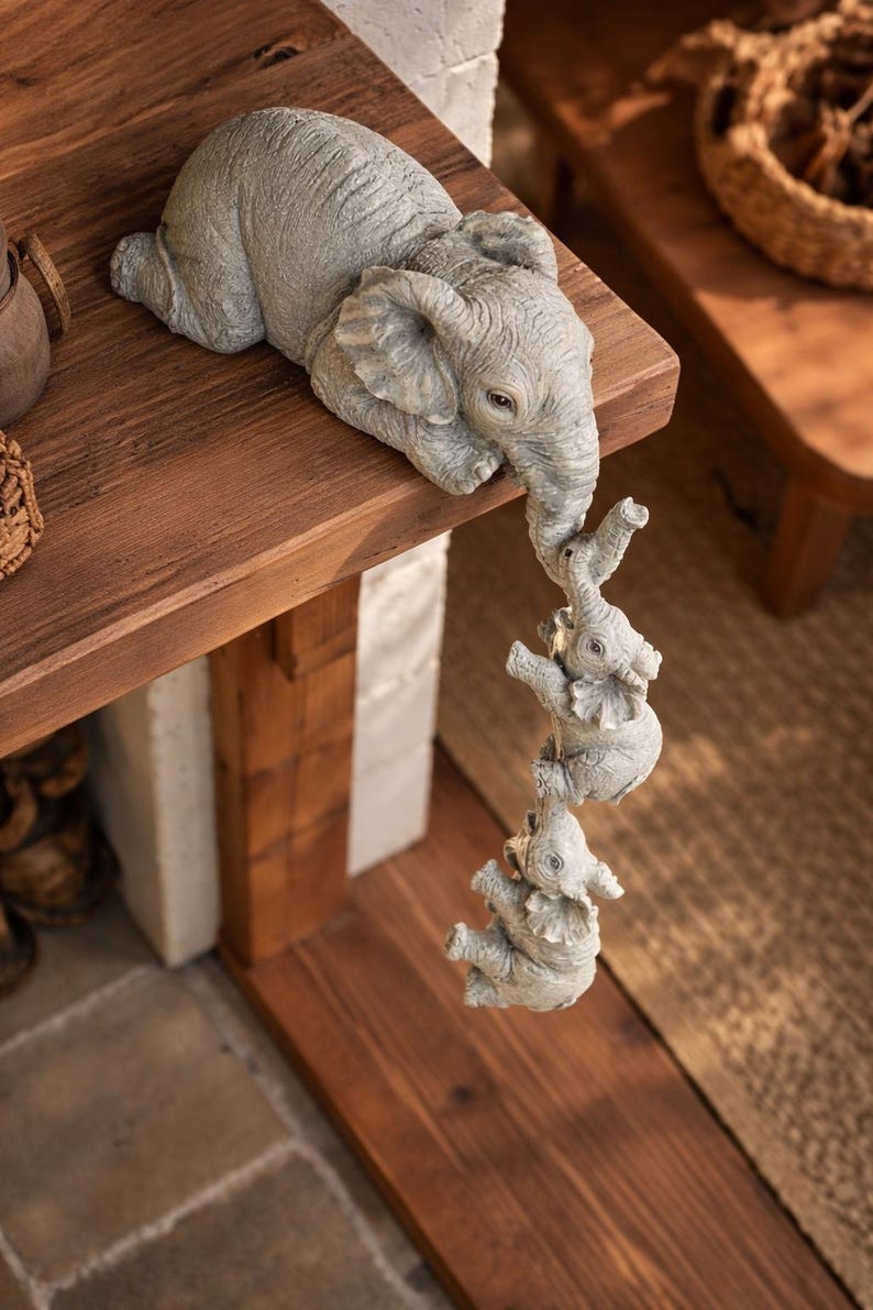 May include: A gray elephant figurine with three smaller elephants hanging from its trunk. The elephants are on a wooden shelf. The figurine is a decorative item.