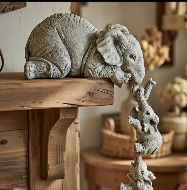 May include: A gray elephant figurine with three smaller elephants stacked below. The largest elephant rests on a wooden shelf, while the smaller ones are balanced on top of each other. The figurine has a textured surface and is a decorative item.