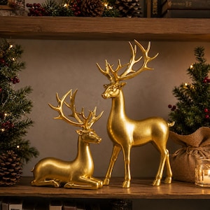 Peut inclure: Deux figurines de cerf de couleur dorée avec de grands bois détaillés. Un cerf est en position allongée avec les pattes repliées en dessous, tandis que l'autre cerf se tient debout sur ses quatre pattes. Les deux ont une finition métallique.