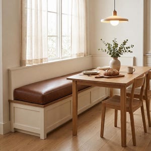May include: A dining set featuring a rectangular wooden table, a long built-in bench with a brown leather cushion, and wooden chairs. A ceramic vase with green foliage and a loaf of bread sit on the table under a modern wooden pendant light.