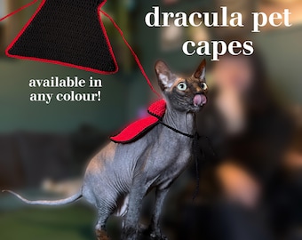 Puede incluir: Un gato Sphynx con una capa de Drácula de ganchillo roja y negra. La imagen incluye el texto "crochet Dracula pet capes" y "available in any colour!". La capa está conectada a una correa a juego.