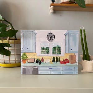 May include: An illustration of a kitchen scene with light blue cabinets, a window, and a disco ball. The countertop displays vegetables, a radio, and a paper bag. A potted plant and a ceramic candle holder with green candles are on the right.