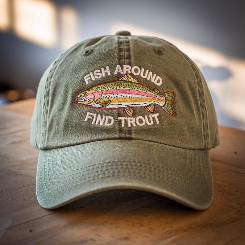 May include: Olive green baseball cap with the embroidered text "FISH AROUND FIND TROUT" and a colorful trout illustration. The hat has a curved brim and a classic six-panel design, perfect for outdoor activities.