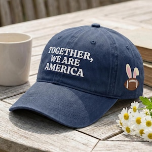 May include: Navy blue baseball cap with the text "TOGETHER, WE ARE AMERICA" in white. The cap features an embroidered football with bunny ears. A casual accessory for everyday wear.