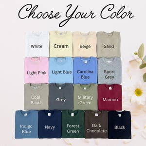 May include: A collection of fifteen crewneck sweatshirts arranged in a grid, each labeled with its color: White, Cream, Beige, Sand, Light Pink, Light Blue, Carolina Blue, Sport Grey, Cool Sand, Grey, Military Green, Maroon, Indigo Blue, Navy, Forest Green, Dark Chocolate, and Black. The text 'Choose Your Color' is at the top.