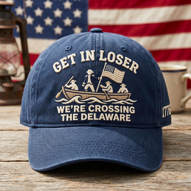 K&ouml;nnte beinhalten: Marineblaue Baseballkappe mit dem Text "GET IN LOSER" &uuml;ber einem Bild eines Bootes, das den Delaware River &uuml;berquert. Der Text "WE'RE CROSSING THE DELAWARE" befindet sich unter dem Boot. Das Jahr "1776" ist auf der Seite.