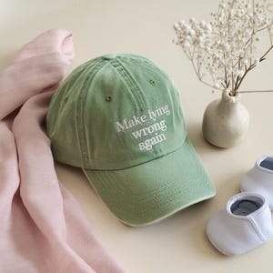 May include: A green baseball cap with the text "Make lying wrong again" embroidered in white on the front.