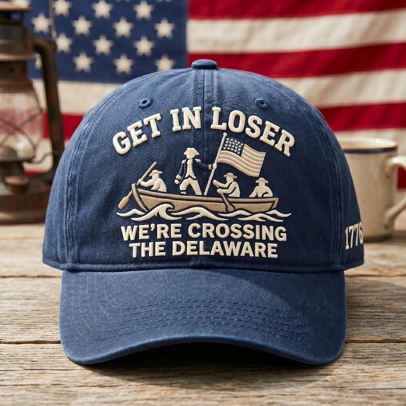 K&ouml;nnte beinhalten: Marineblaue Baseballkappe mit dem Text "GET IN LOSER" &uuml;ber einem Bild eines Bootes, das den Delaware River &uuml;berquert. Der Text "WE'RE CROSSING THE DELAWARE" befindet sich unter dem Boot. Das Jahr "1776" ist auf der Seite.