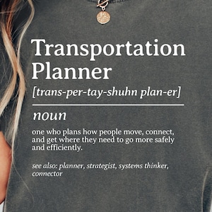 May include: Dark gray unisex t-shirt with the text "Transportation Planner" in white. The definition of the term is also included. The shirt is a comfortable, casual style.