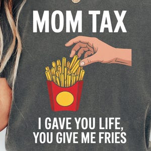 以下が含まれることがあります： 「MOM TAX」の文字と、フライドポテトを掴む手のグラフィックがプリントされた、ペッパーカラーのユニセックスTシャツ。「I GAVE YOU LIFE, YOU GIVE ME FRIES」の文字が下にプリントされています。