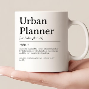 Może przedstawiać: Biały ceramiczny kubek z czarnym napisem "Urban Planner". Kubek zawiera również wymowę fonetyczną i definicję terminu. Jest trzymany w dłoni i ma zakrzywiony uchwyt. Tło jest neutralne.