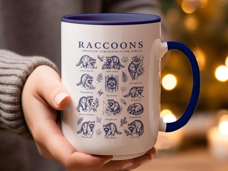 White mug with navy blue rim and handle featuring diverse raccoon illustrations and text.
