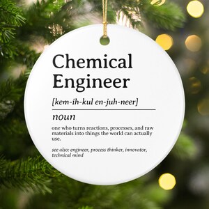 May include: A white, round Christmas ornament with the words "Chemical Engineer" in bold black text. Below the title is the phonetic pronunciation and a definition. The ornament hangs from a gold string.