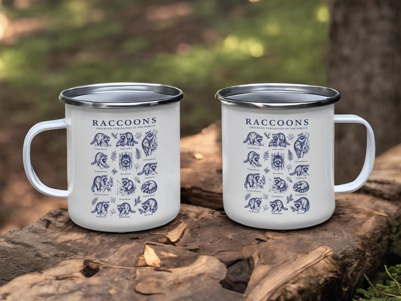 Two white enamel mugs with blue raccoon illustrations and text.