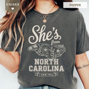 Dark grey t-shirt with "She's from North Carolina" and floral outline of state.