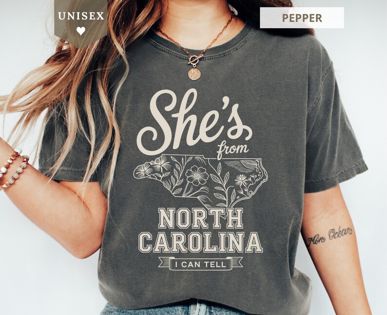 Dark grey t-shirt with "She's from North Carolina" and floral outline of state.