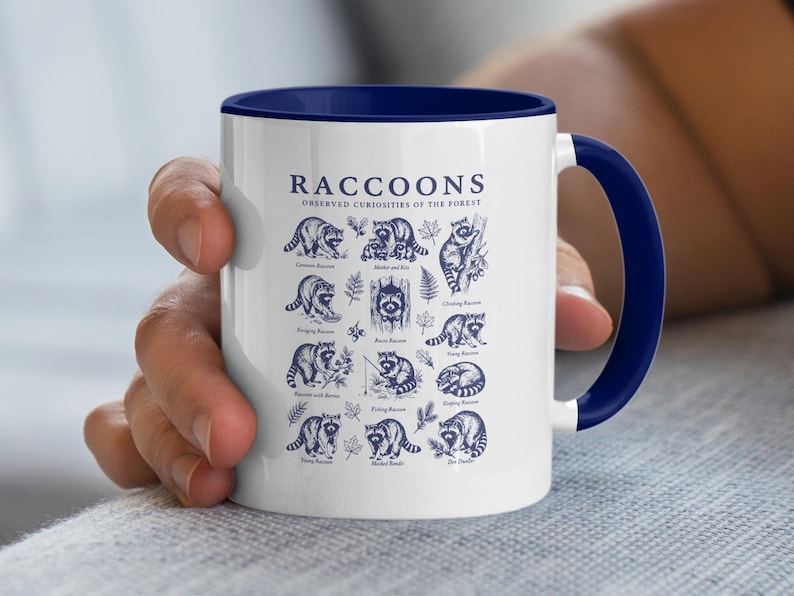 White mug with blue trim featuring a collage of raccoon illustrations and labels.