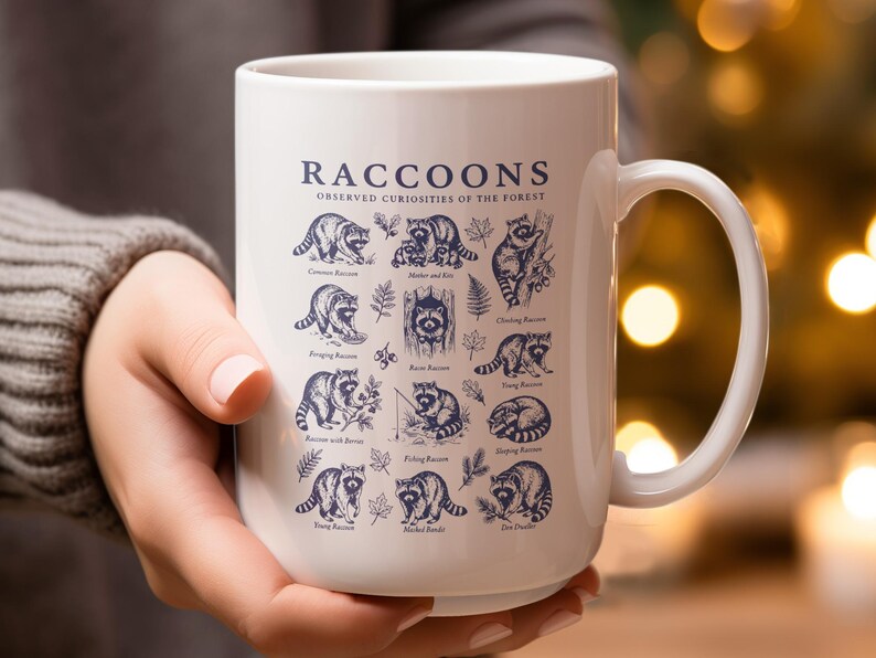 White mug with "Raccoons Observed Curiosities of the Forest" and raccoon illustrations.