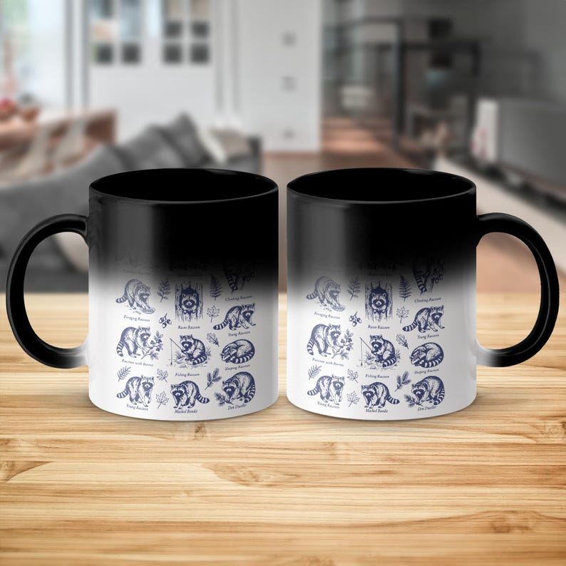 Two black ceramic mugs with navy blue illustrations of raccoons in various poses.