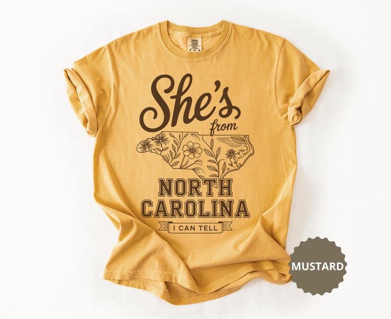 Mustard t-shirt with floral outline of North Carolina and "She's from North Carolina I can tell" text.