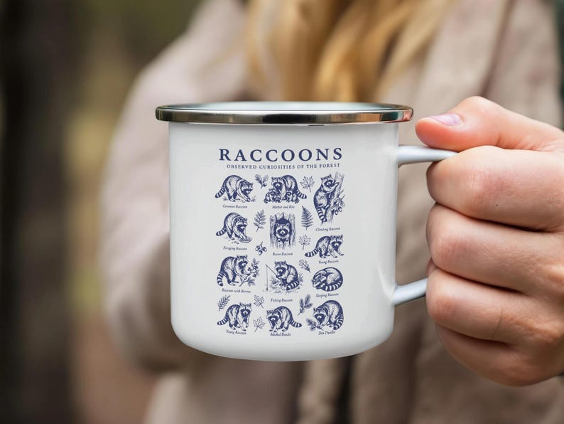 White enamel mug with dark blue illustrations and text about raccoons observed in the forest.
