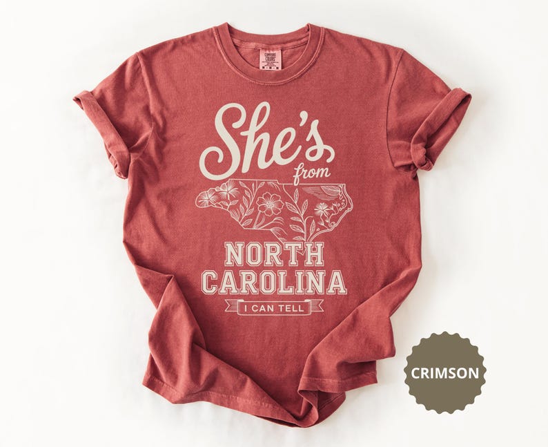 Crimson t-shirt with "She's from North Carolina" and floral outline of the state.