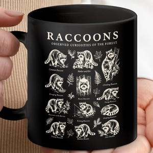 Black mug with cream-colored raccoon illustrations and labels, each showing different raccoon activities.
