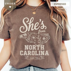 Brown unisex t-shirt with "She's from North Carolina" and floral design.