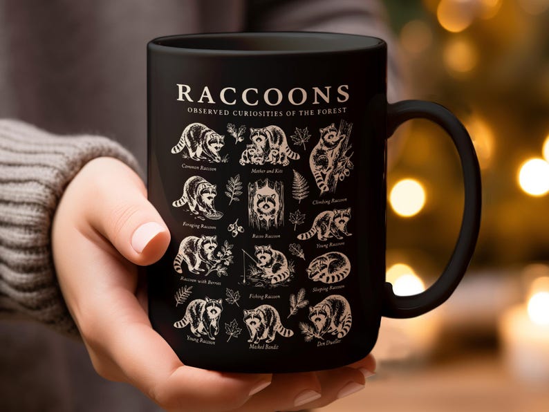 Black mug with raccoon illustrations and "Raccoons Observed Curiosities of the Forest" text.