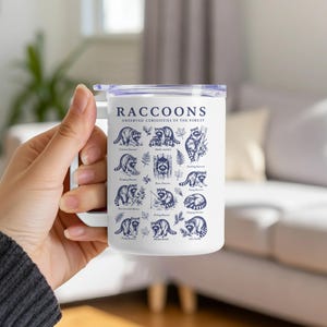 White mug with navy blue illustrations and text of various raccoons and labels.