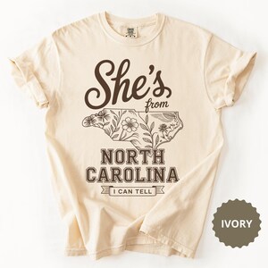 Cream t-shirt with "She's from North Carolina I Can Tell" text and floral outline.
