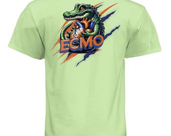 Può includere: T-shirt verde chiaro con una grafica di un alligatore verde che tiene un cuore umano. Il design include la parola "ECMO" in arancione e blu, con artigli arancioni e blu. La maglietta è realizzata in materiale morbido.