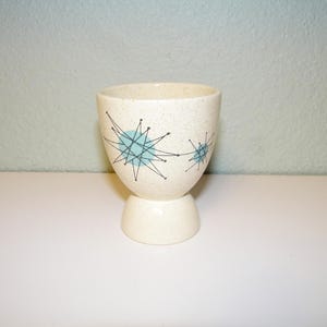 May include: White ceramic egg cup with a blue and black starburst design.