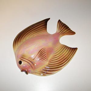 May include: A ceramic wall plaque shaped like an angelfish with an iridescent pink and cream body. The fins and tail feature brown striped detailing, and the fish has a dark brown eye and a small, slightly open mouth facing toward the left.