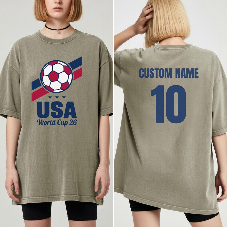 Puede incluir: Camiseta verde oliva con un gr&aacute;fico de bal&oacute;n de f&uacute;tbol, rayas rojas y azules, y el texto "USA" y "World Cup 26". La parte trasera muestra "CUSTOM NAME" sobre el n&uacute;mero "10" en azul.