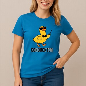 T-shirt featuring a cartoon duck wearing sunglasses and a bow tie, holding a conductor’s baton, with the word “CONDUCKTOR” printed below as a music pun.